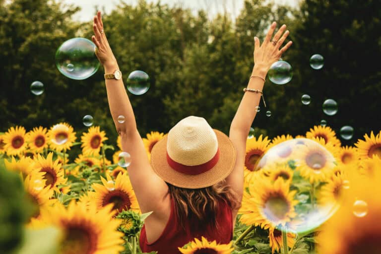 A women with a hat with arms up in the air in the field of sunflowers